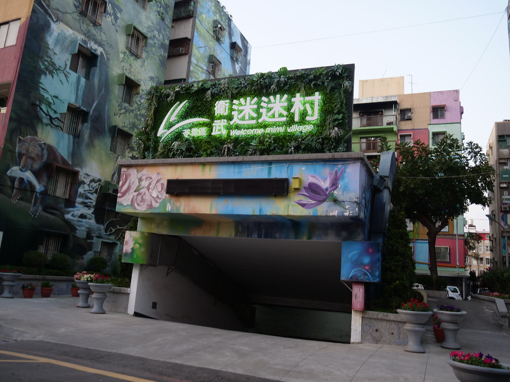 衛武迷迷村綠色入口招牌與後方森林壁畫住宅